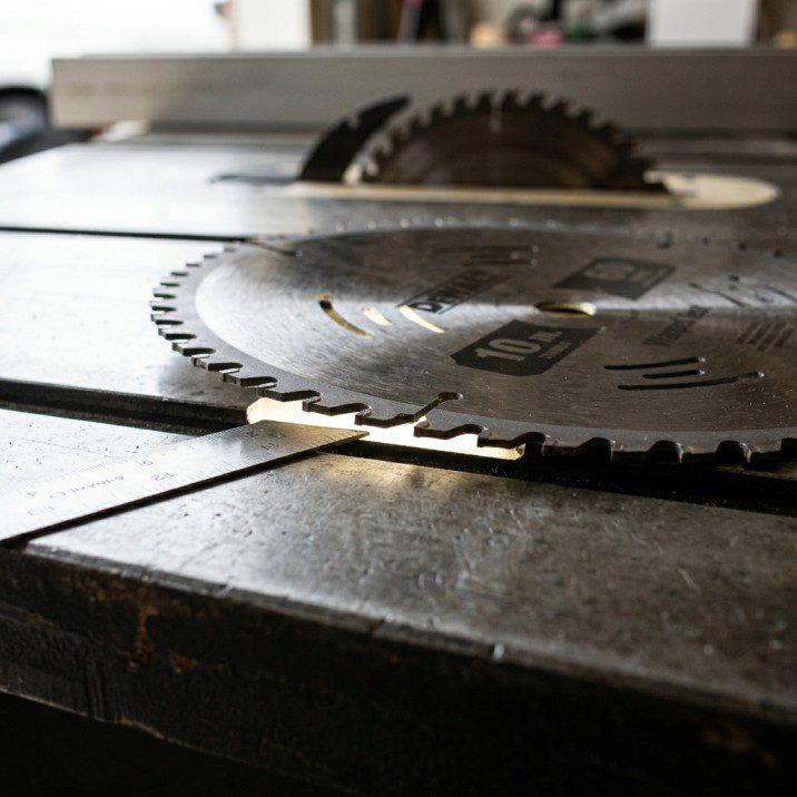 Warped table saw blade lying on cast iron surface showing visible gap under the rim — bent blade causing wobble
